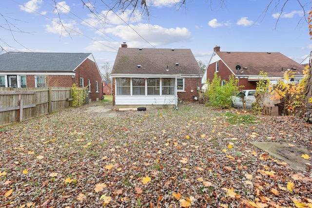 rear view of house with a sunroom, brick siding, and fence