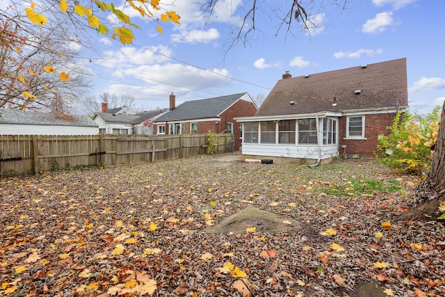 back of house with a chimney, a sunroom, brick siding, and a fenced backyard