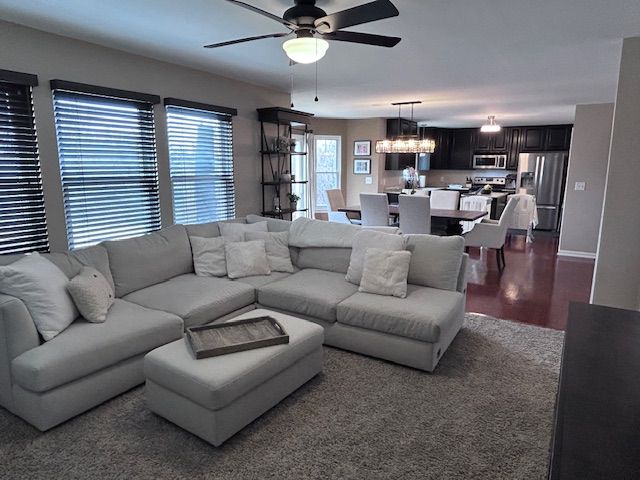 living room featuring dark wood-style flooring, baseboards, and ceiling fan with notable chandelier