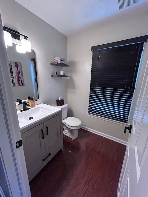 half bathroom featuring toilet, wood finished floors, vanity, visible vents, and baseboards