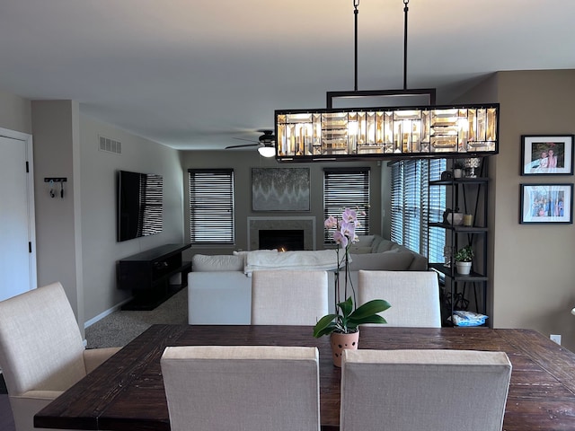 living area with baseboards, visible vents, a ceiling fan, a lit fireplace, and dark carpet