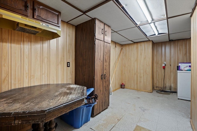 interior space with light floors, a drop ceiling, washer / dryer, and wooden walls