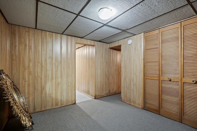 interior space featuring carpet flooring, wooden walls, and a drop ceiling