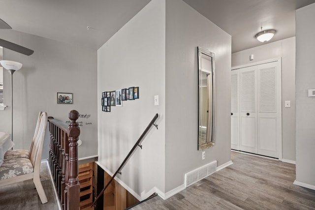 corridor featuring baseboards, visible vents, an upstairs landing, and wood finished floors