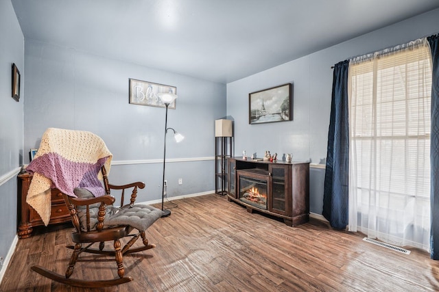 living area with a glass covered fireplace, visible vents, baseboards, and wood finished floors