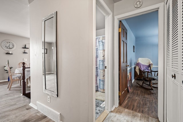 hallway featuring visible vents, baseboards, and wood finished floors