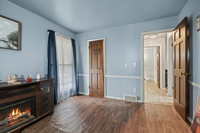 bedroom featuring baseboards, a lit fireplace, visible vents, and wood finished floors