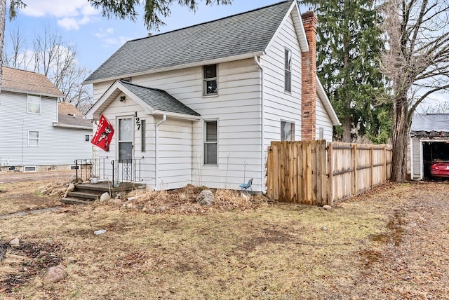 view of front of house with a shingled roof, a chimney, and fence