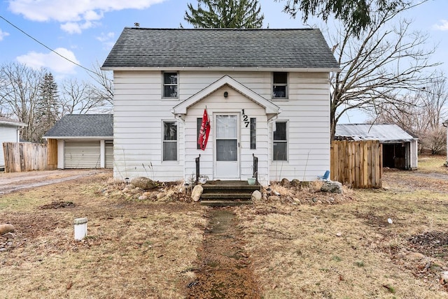 colonial home featuring a shingled roof, an outbuilding, and fence