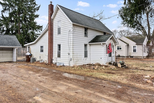 view of front facade featuring a chimney, central AC unit, and roof with shingles