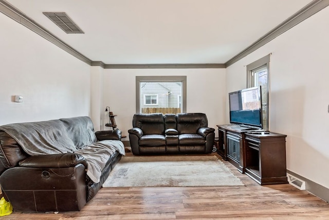 living room with light wood-type flooring, visible vents, and crown molding