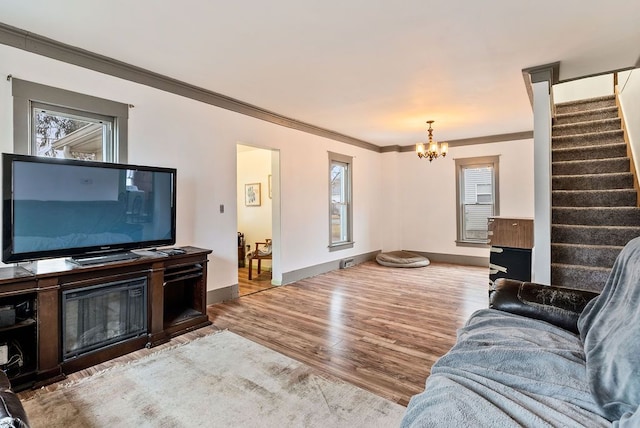 living room with wood finished floors, baseboards, stairs, ornamental molding, and an inviting chandelier