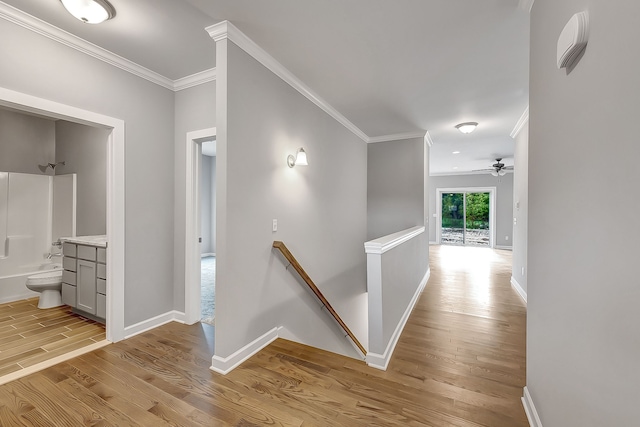 corridor with light wood-style flooring, baseboards, crown molding, and an upstairs landing