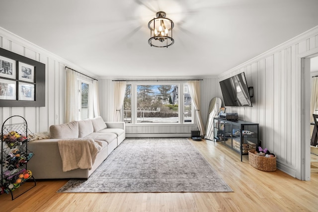 living area featuring a notable chandelier, baseboard heating, crown molding, and wood finished floors