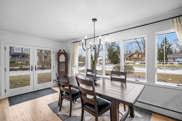 dining area featuring a notable chandelier, french doors, baseboard heating, and light wood-style floors