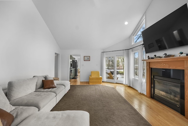 living area with light wood-style floors, a glass covered fireplace, high vaulted ceiling, and recessed lighting