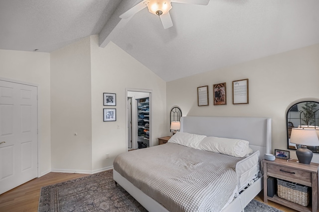 bedroom featuring baseboards, lofted ceiling with beams, ceiling fan, wood finished floors, and a walk in closet