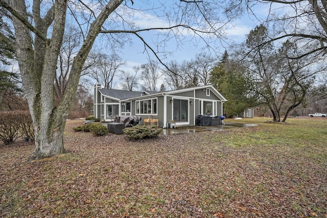 view of front facade featuring a sunroom, a patio area, a chimney, and a front lawn