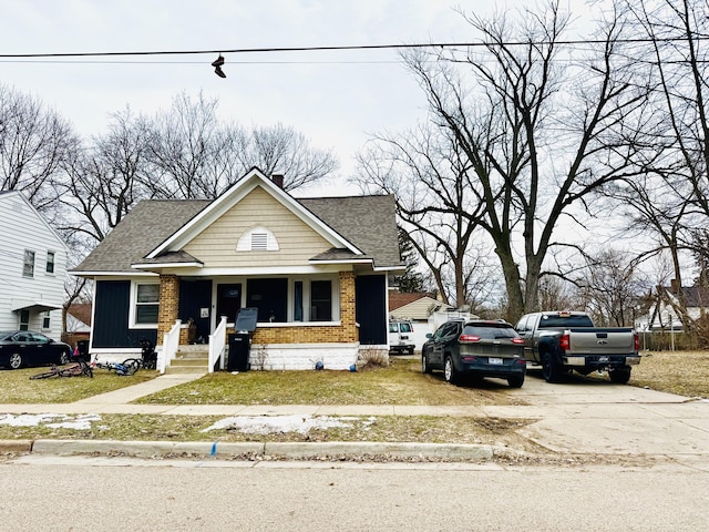 bungalow with covered porch, brick siding, driveway, and roof with shingles