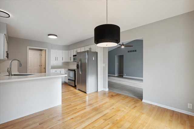 kitchen with stainless steel appliances, a peninsula, a sink, white cabinetry, and light wood finished floors