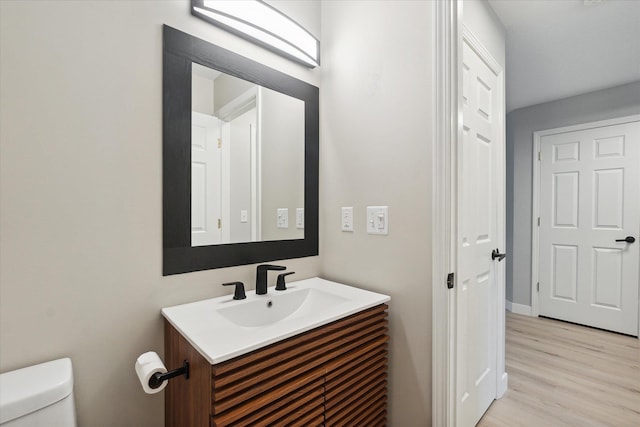 half bath featuring wood finished floors, vanity, and toilet