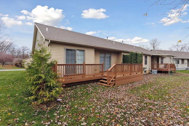 back of house featuring roof with shingles, a lawn, and a wooden deck