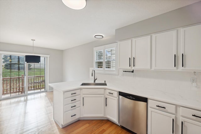 kitchen with stainless steel dishwasher, light wood-style floors, white cabinets, a sink, and a peninsula