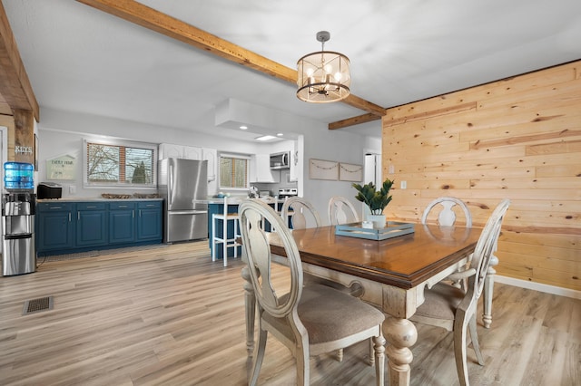 dining room featuring light wood finished floors, wooden walls, a chandelier, and beam ceiling