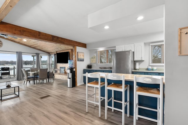 kitchen featuring plenty of natural light, freestanding refrigerator, white cabinetry, and vaulted ceiling with beams