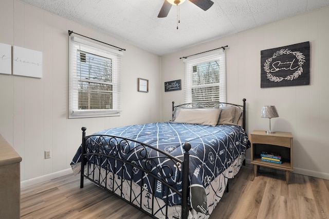 bedroom with ceiling fan, a textured ceiling, baseboards, and wood finished floors