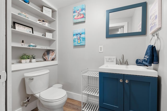 half bathroom featuring toilet, baseboards, wood finished floors, and vanity