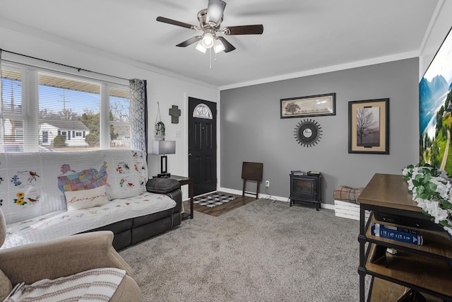 living room with baseboards, a ceiling fan, a wood stove, crown molding, and carpet flooring