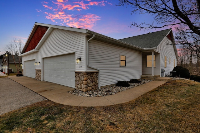 property exterior at dusk with an attached garage, stone siding, and concrete driveway