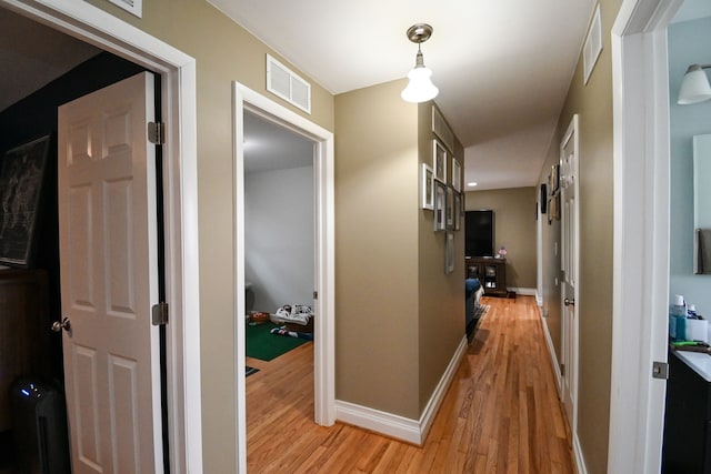 hallway featuring visible vents, light wood-style flooring, and baseboards