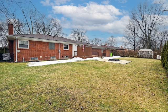 rear view of property featuring an outdoor fire pit, a chimney, fence, a yard, and brick siding