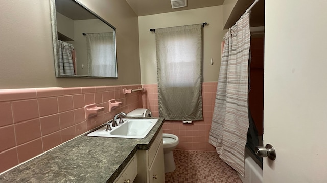 full bathroom with visible vents, toilet, vanity, wainscoting, and tile walls