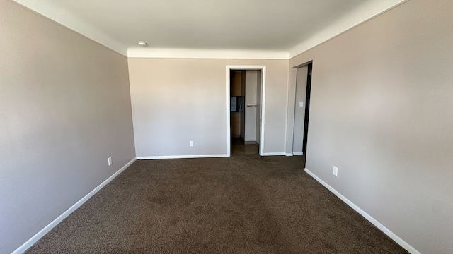 unfurnished room with baseboards and dark carpet