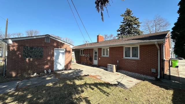 back of house featuring a lawn, brick siding, central AC, and a chimney