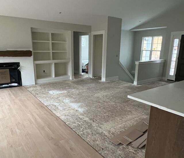 unfurnished living room with built in shelves, a fireplace, vaulted ceiling, and wood finished floors