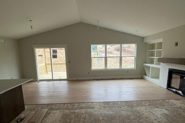 unfurnished living room featuring vaulted ceiling, wood finished floors, a glass covered fireplace, and built in features