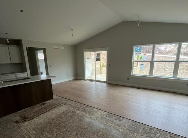 interior space featuring open floor plan, white cabinets, vaulted ceiling, light wood-type flooring, and baseboards