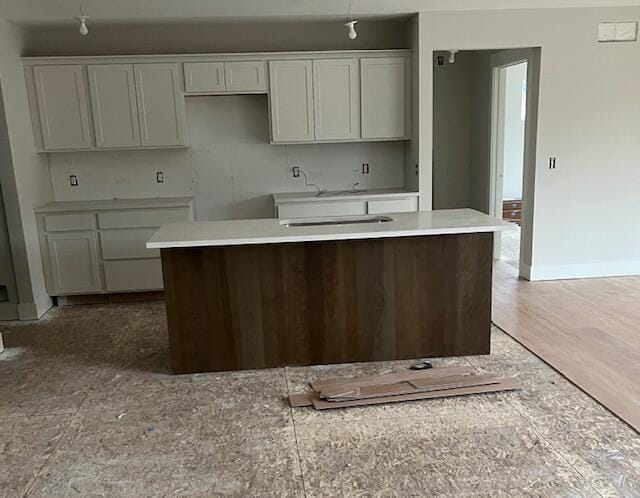 kitchen with light wood-type flooring, a kitchen island with sink, baseboards, and white cabinetry