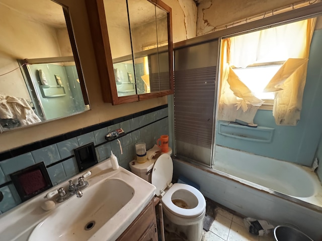 bathroom featuring toilet, shower / bath combination with glass door, tile walls, vanity, and tile patterned floors