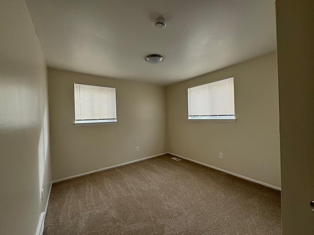 unfurnished room with carpet, visible vents, and baseboards