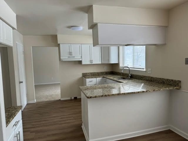 kitchen with a peninsula, stone counters, white cabinets, and a sink