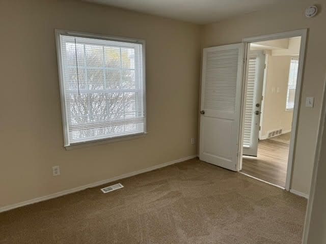 unfurnished room featuring plenty of natural light, carpet flooring, visible vents, and baseboards