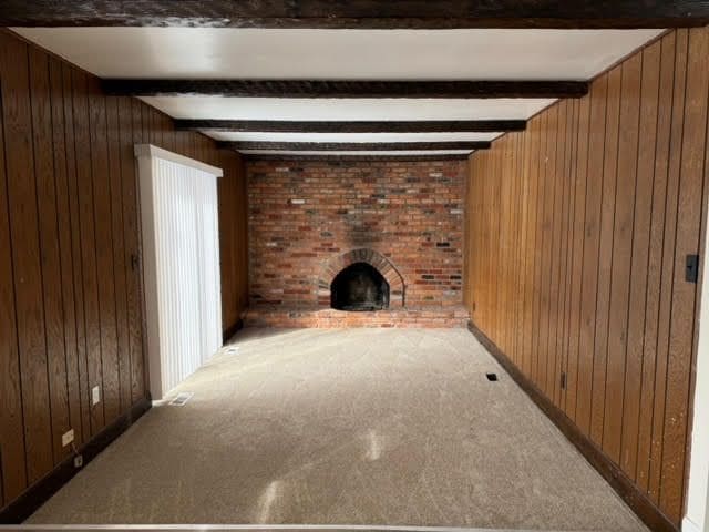 unfurnished living room featuring a brick fireplace, beamed ceiling, carpet, and wooden walls