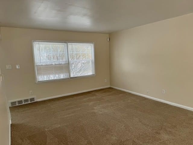 empty room with carpet floors, baseboards, and visible vents