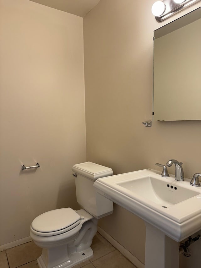 half bath with toilet, baseboards, and tile patterned floors