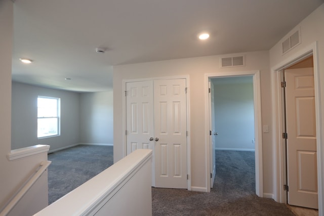 corridor featuring visible vents, dark carpet, and an upstairs landing